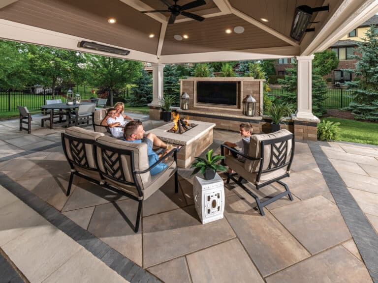 Covered backyard patio designed as an outdoor living room with seating, a fireplace and a dining area.
