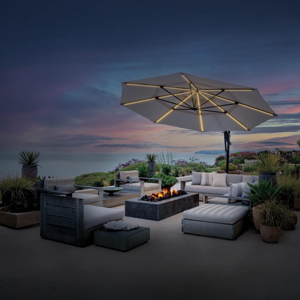 Umbrella with lighting underneath over fire table and patio furniture at dusk